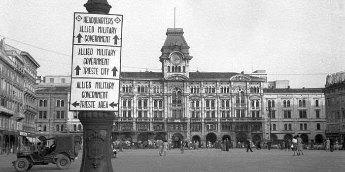 Fotografija iz filma \&quot;Our American Days\&quot;, prikazuje znak z napotki do različnih lokacij. V ozadju je Tržaška mestna hiša v Trstu.